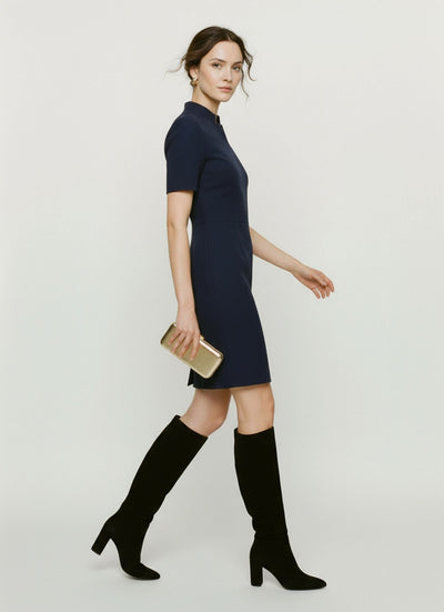 Woman wearing a navy dress with knee-high black boots on a white background