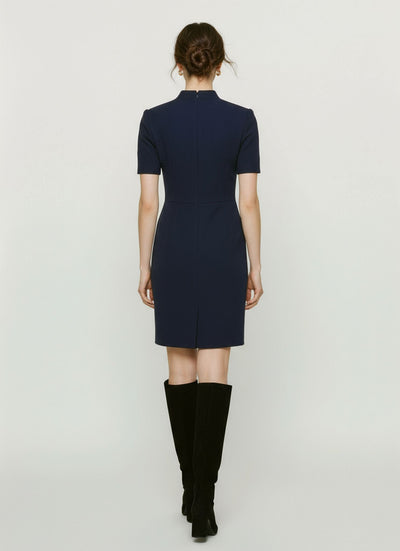 Woman wearing a navy blue dress with knee-high black boots on a light gray background