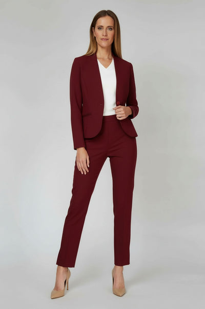 A woman modeling a burgundy two-piece blazer and trouser set with a white V-neck top and beige heels, standing against a light gray studio background.