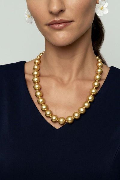Woman wearing a gold pearl necklace against a neutral background