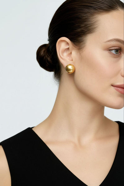 Woman wearing gold earrings against a light gray background